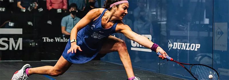 A pro squash player reaching for a ball